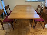 Front view of wooden dining table in closed (square) configuration with chairs around.