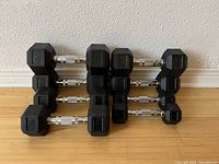 Eight black hex dumbbells arranged in front of wall, stacked in two rows