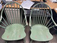 Front top view of two green wooden chairs showing spindle backs, arm rests, and worn green paint with surface scratches
