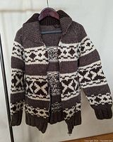 Front view hanging on hanger showing front knit pattern, zipper partially zipped, wide collar and sleeve details.