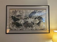 Photo showing the large framed black and white floral artwork hanging on a wall with a lamp beside it.