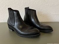 Pair of black leather Chelsea boots showing left and right side profiles, highlighting elastic side panels and pull tabs at the back.