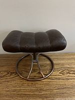 Top angled view of the vintage leather footstool showing three cushioned segments and metal circular base.