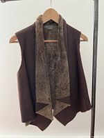Front view of brown shearling vest on hanger showing draped collar and asymmetrical front edges.