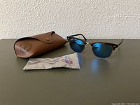 Full view of sunglasses with mirrored blue lenses, tortoise shell frame, brown Ray-Ban case, and cleaning cloth.