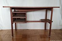 Front view of mid century teak desk showing open shelving section on left with missing drawers and small shelf attached to right leg.