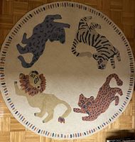 Full view of round rug showing four safari animals (lion, zebra, leopard, elephant) around the perimeter on a beige background with multicolor dashed edge.
