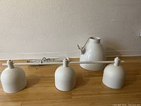 EQ3 metal fixture with three white bell-shaped luminaires arranged linearly, lying horizontally with visible cable and plug.