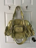 Front view of purse showing multiple zippered and buttoned external pockets, silver-tone rings and rivets, and dual top handles.