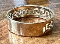 Wide view of ring on wooden surface showing Greek key cutout pattern and polished finish