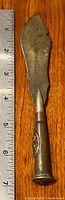 Full length view of metal letter opener with ruler for scale, showing approx 6.5 inches length and broad asymmetrical blade.