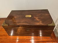 Closed exterior view of antique wooden writing box with brass corners and a lock plate