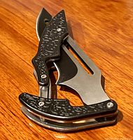 Folded knife on wooden surface showing distinct scrollwork on handle and part of the stainless steel blade.