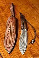 Feather-shaped blade cutter and leather sheath side by side on wooden surface