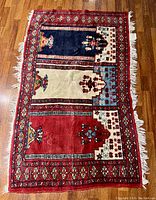 Full view of rug showing three vertical colored panels and the decorative border, placed on wooden floor.