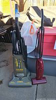 Two vacuum cleaners side by side: a full-sized Eureka SmartVac upright vacuum with True HEPA label and a smaller red Super Broom stick vacuum.