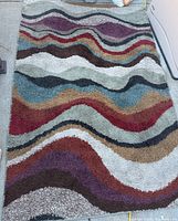 Full view of colorful 5x7 rug with wave pattern in purples, reds, browns, tans, whites and blues.