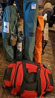 Camping gear items packed in carry bags: green Slumberjack tent, black fabric table, orange and green camp chairs, vintage canteen, and red-black duffel bag