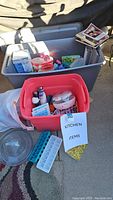 Two storage bins filled with assorted kitchen items including utensils, appliances, and containers; blue and white ice cube trays in front.