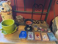 Photo showing ceramic raccoon cookie jar, green flower pot, black wax warmer, assorted tea light candles and 5 different Scentsy wax bar packs on a wooden surface against a red wall with part of a metal art/book stand in background.