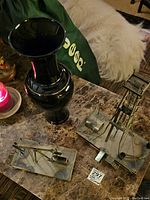 Two metal oil sculptures and tall black vase on table with a dog in background