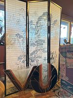 4-panel Asian style room divider screen with painted mountain and tree landscape, standing behind two artistic glass vases with metal bases.