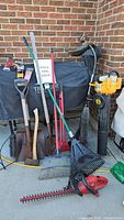 Overview of lot showing various yard tools including rakes, shovels, manual hedge trimmer, bug zapper user tool and covered Traeger grill (not included).