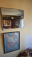 Photo showing uniquely shaped mirror mounted on wall above framed North America map and part of office room.