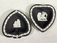 Top view of two Wedgwood black jasperware heart-shaped dishes showing central white relief designs and laurel borders.