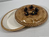 Ceramic covered pie dish with lid featuring five blackbird figurines. The pie dish is cream colored with a brown lid.