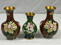 Front view of three Chinese cloisonné vases with floral designs and brass rims in varying sizes.