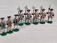 Front view of eight hand-painted French toy soldier figures lined up, showing variety in coat colors and weapons