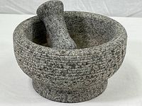 Photo of large solid stone mortar with pestle inside showing rough textured stone surface and shape details.