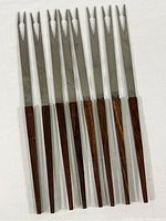 Full view of eight Mid Century Modern fondue forks with wood handles and stainless steel prongs laid side by side.