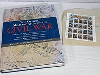 The Official Military Atlas of the Civil War hardcover book shown alongside a sheet of U.S. Civil War commemorative stamps.