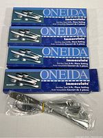 Four boxes of Oneida Immaculate Belmont stainless steel 5-piece place settings stacked, one opened with wrapped flatware pieces visible.