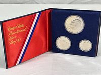 Three silver coins displayed in blue velvet folder with red satin interior, coins dated 1776-1976, protective plastic capsules visible
