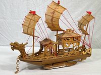Front and full side view of the handcrafted wooden Chinese dragon boat with three bamboo sails and dragon head bow, resting on wooden base