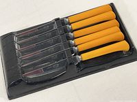 Set of six steak knives with yellow bakelite handles in a black lightweight plastic storage rack.