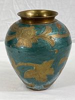 Front side of the brass vase showing floral design on dusty teal surface with some visible wear and fading.