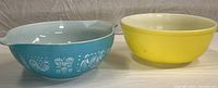 Side view showing blue Pyrex Amish Butterprint bowl with white decorative folk art and yellow Pyrex 404 bowl