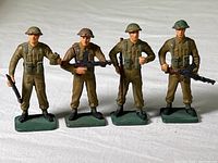 Four vintage U.S. WW1 toy soldier figures standing in a row, showing different poses and holding rifles, each on a green base