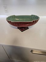 Side angle of vintage ceramic fruit bowl showing green glazed interior, brown exterior with vertical drip pattern, and pedestal base.
