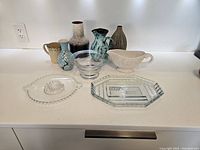 All 10 mixed media decorative and functional pieces including vases, glassware, and serveware shown on white countertop.