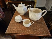Full view of 6-piece white ceramic Lennox beverage set with embossed leafy pattern and gold trim on a wooden table.