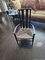 Front view of vintage child's wood chair with rush seat and armrests, showing general structure and seat condition.