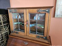Front view of closed oak spice cupboard showing stained glass doors and metal hinge hardware