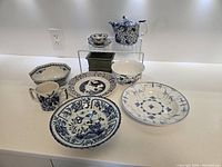 11 pieces of Oriental inspired blue and white porcelain displayed, including plates, bowls, cup, and teapot on display stand.