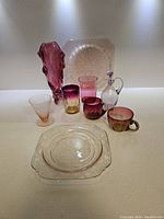 Full lot overview showing all nine pieces including glasses, vases, plates, and decanter in cranberry and clear glass.