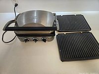 Front view of the Cuisinart electric grill with the lid closed and two ribbed removable plates placed beside it.